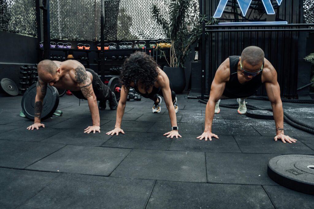 Three individuals performing push-ups together in a Mexico City gym setting.