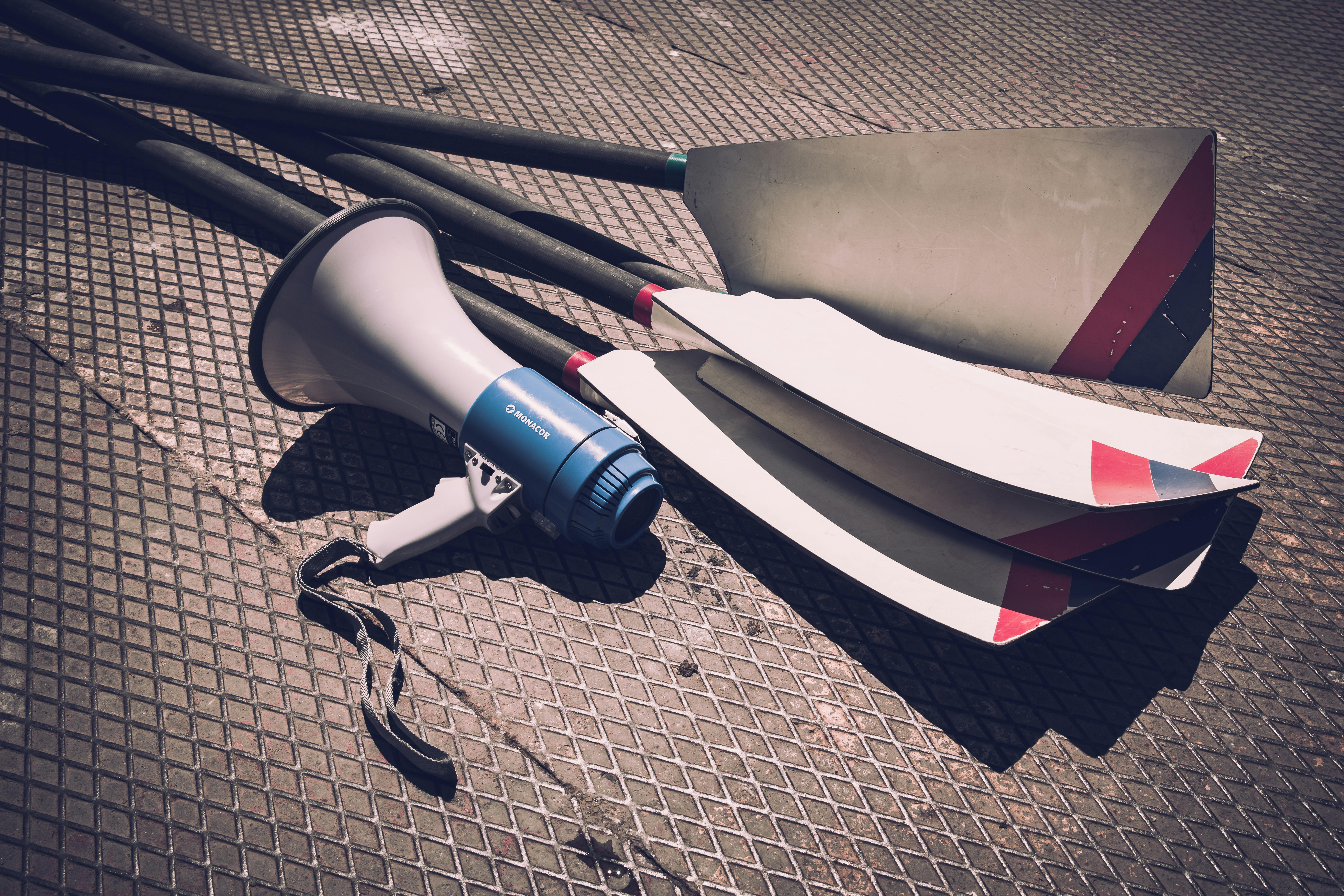 Close-up of a megaphone and rowing oars lying on a sunlit metal ground, showcasing sports gear.