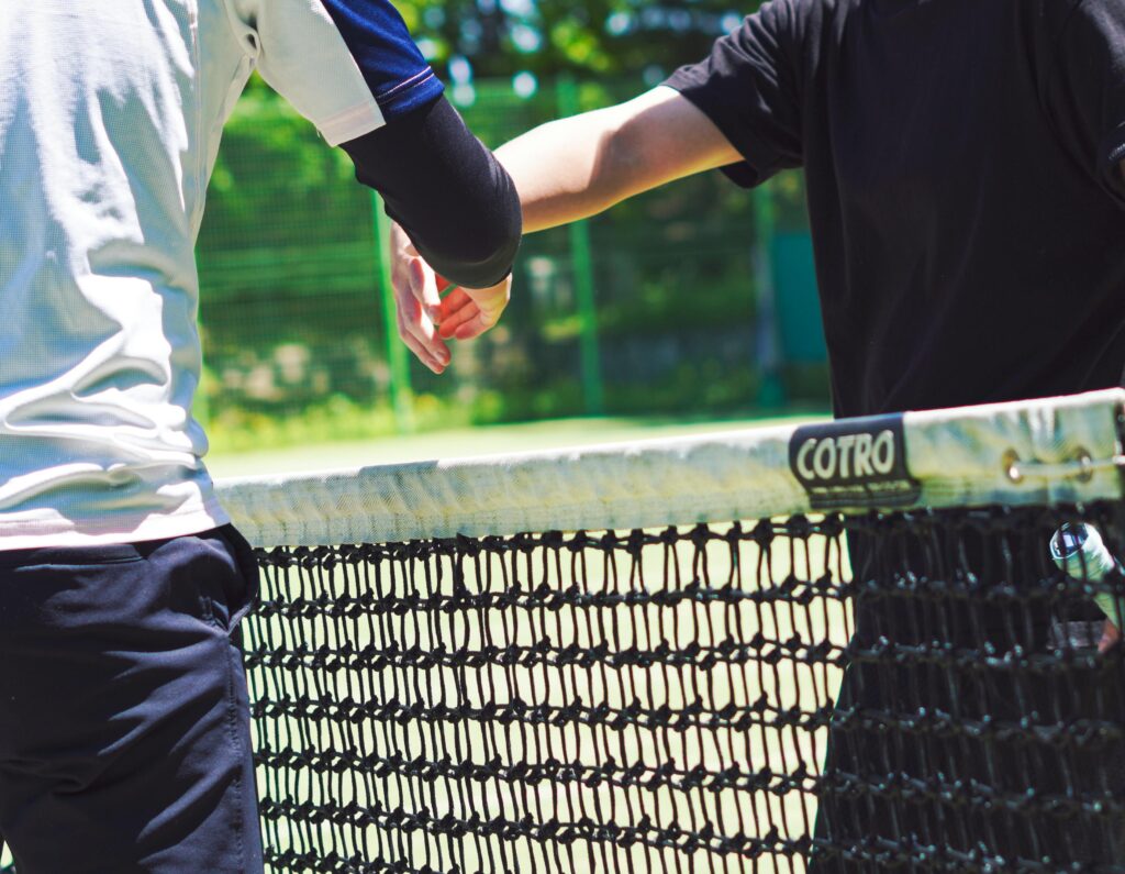 Two tennis players engaging in sportsmanship with a handshake over the net outdoors.