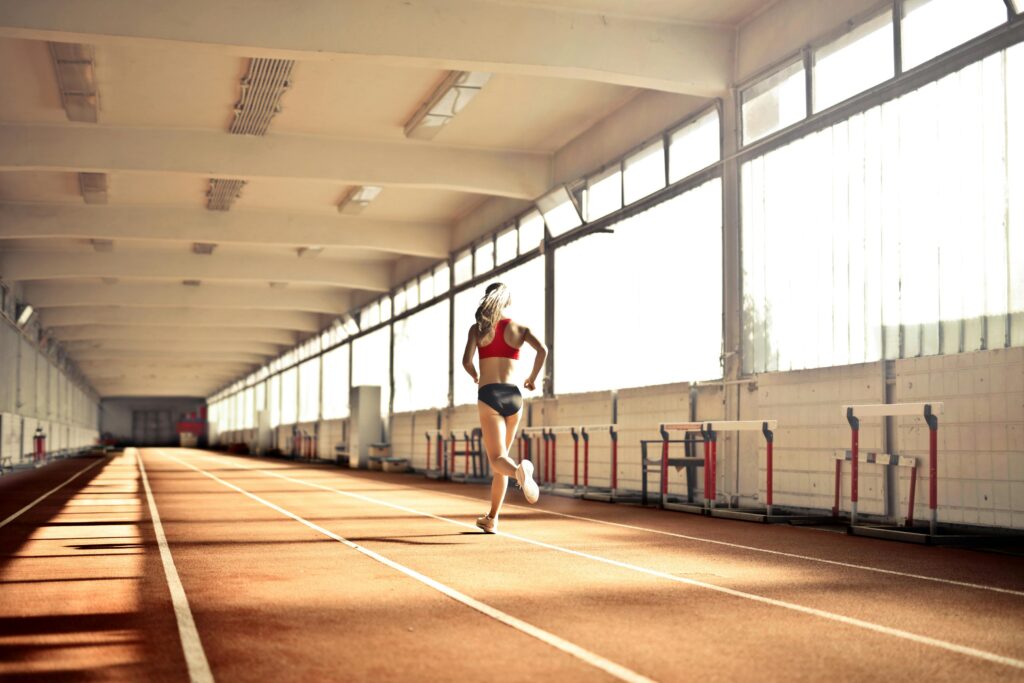 Woman in athletic wear running on an indoor track, showcasing speed and determination.